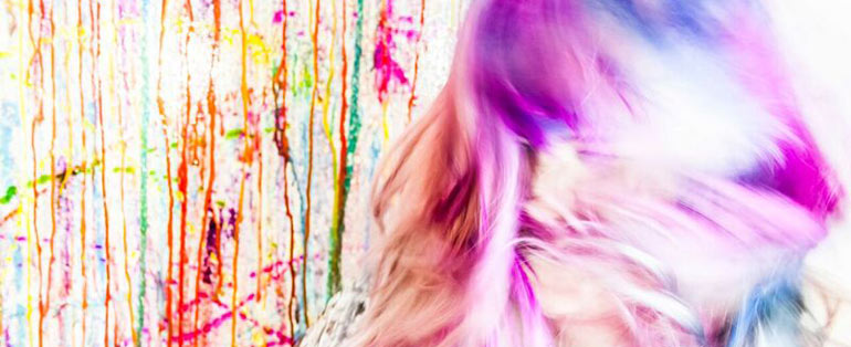 image of person with pink hair against a bright paint splattered background