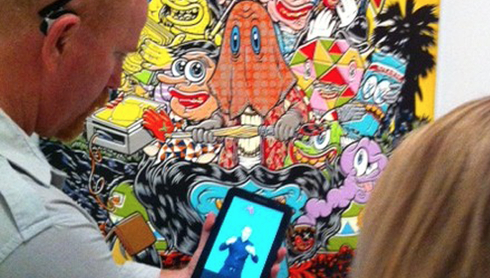 A man stands in front of a colourful artwork with his mobile phone in front of him, watching an accessible Auslan interpretation of it