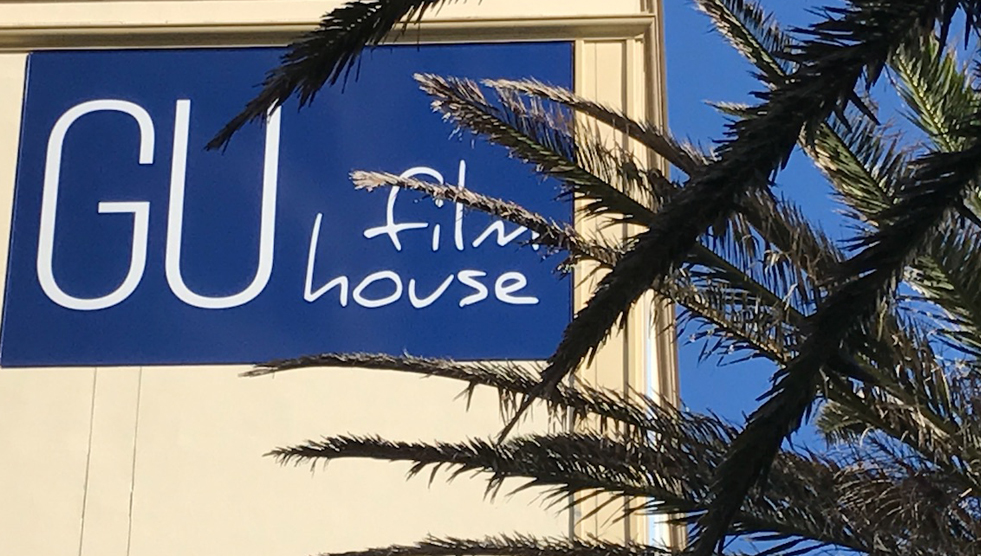 The side of the Gu Film House; a blue sign reads GU film house. Trees to the right