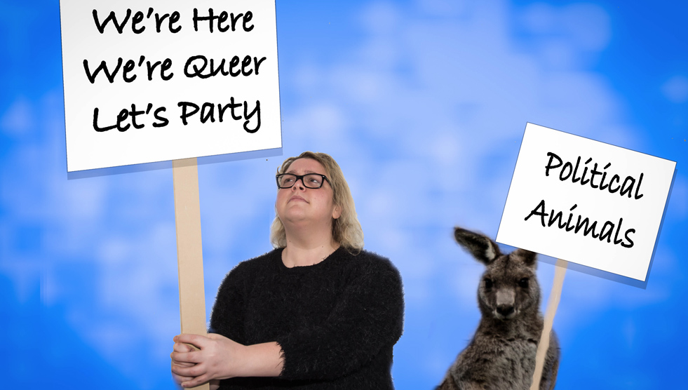 Image of Felicity Nicol: a woman is holding a sign that says "We're here, we're queer, let's party." A kangaroo is holding a sign that says "Political animals."