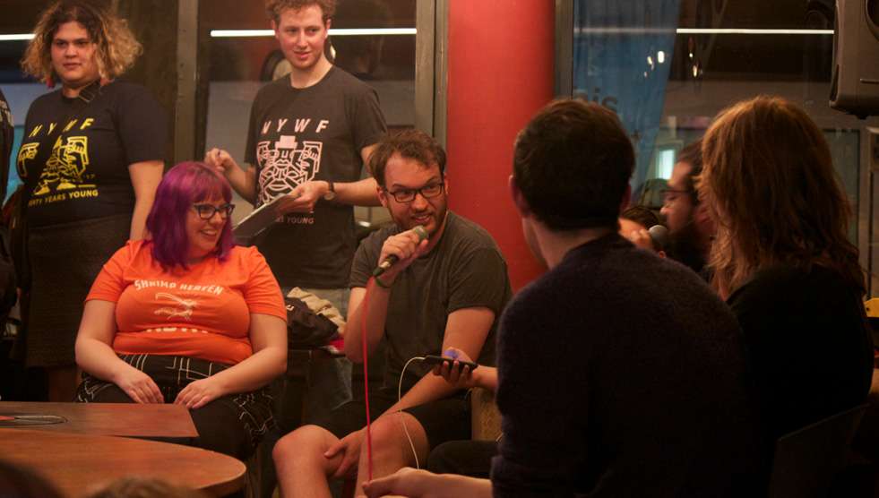 Alistair Baldwin: A person has a microphone and a group of people and sitting and standing around
