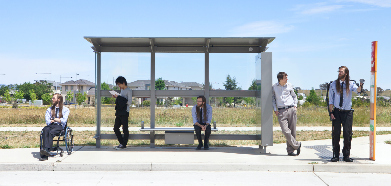 Image of five people waiting at a bus stop. There is an open field behind them.
