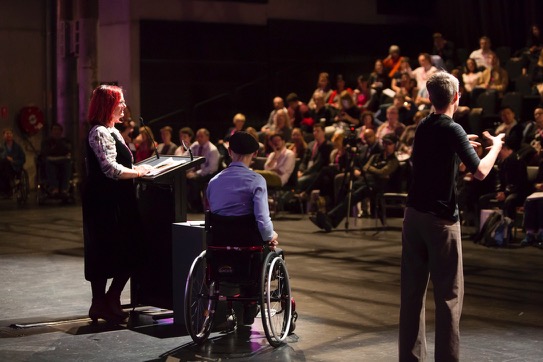 Three presenters on stage at the Arts Activated 2019 Conference - one in a wheelchair. The group is standing in front of an audience.
