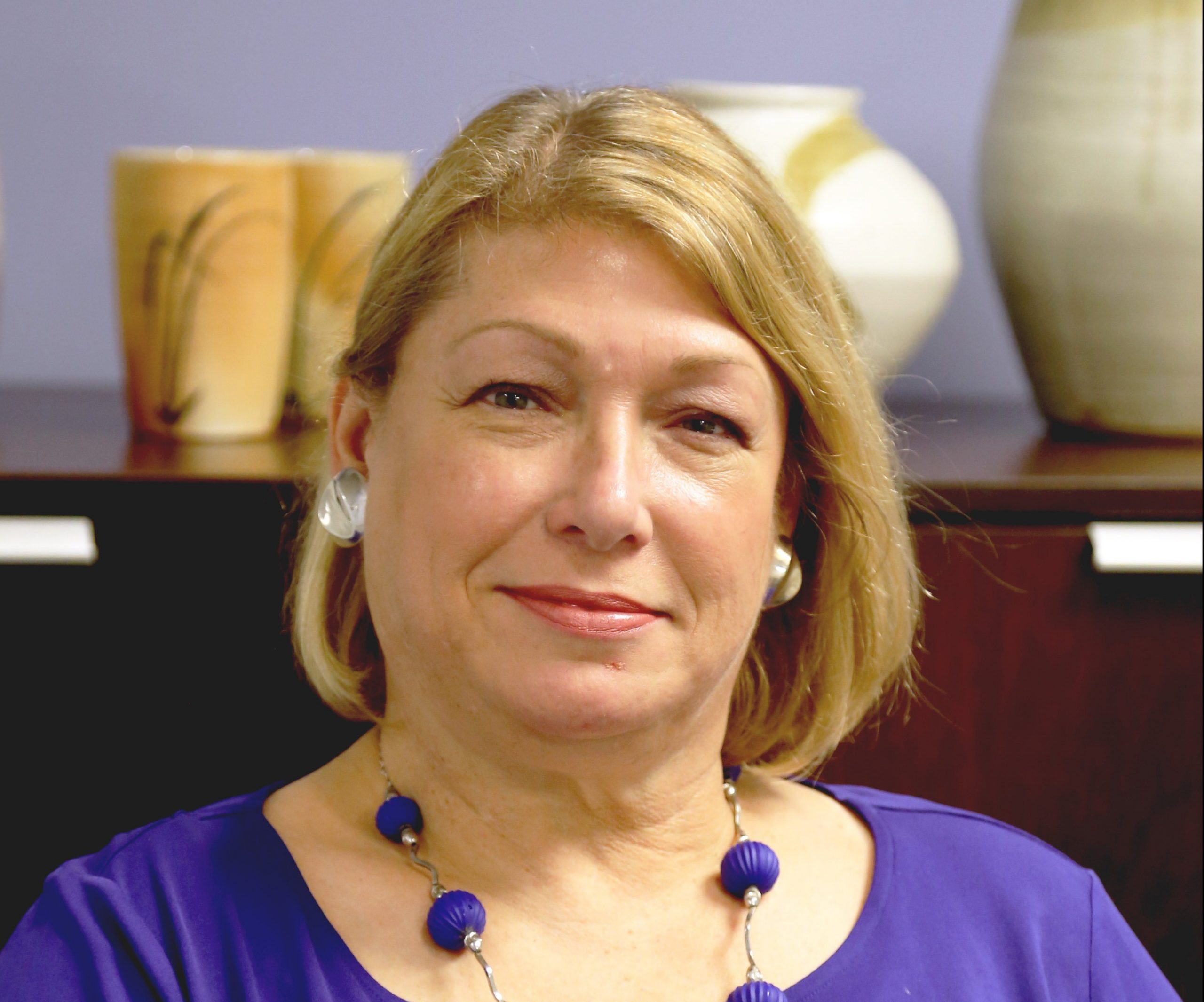 Image of Beth Ziebarth in a purple top sitting in front of a brown cupboard.