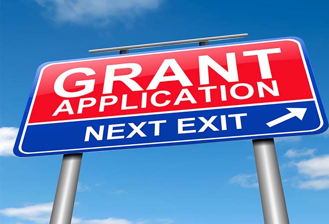 A street sign with the word 'Grant Application Next Exit' set against a blue sky.