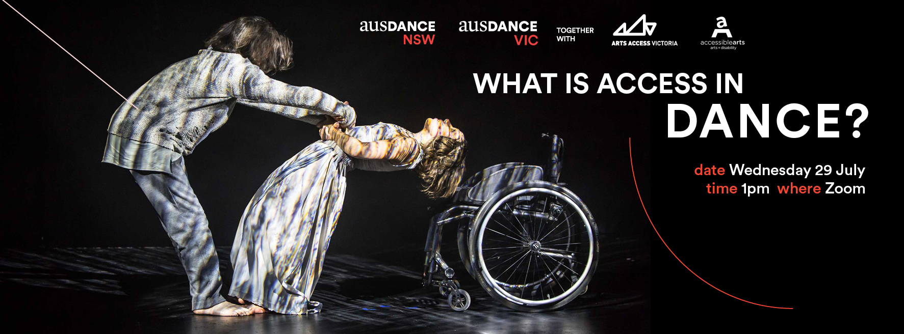 Two dancers are intertwined together through their arm movements. From the left the dancer is bent over with his arms stretched downwards and they are linked with the hands of the dancer on the right. Her head is facing upwards with her body leaning backwards. To the right of the image is a wheelchair. Coloured image on a blacked-out stage, stage lighting shining on the artists.