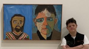 A man is standing next to a portrait of 2 men in a gallery